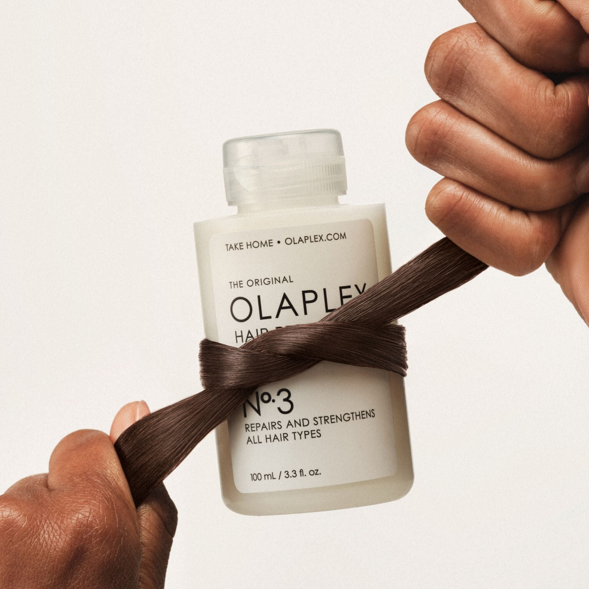 Hair pulled tight around a bottle of OLAPLEX No.3, showing the strength of the hair