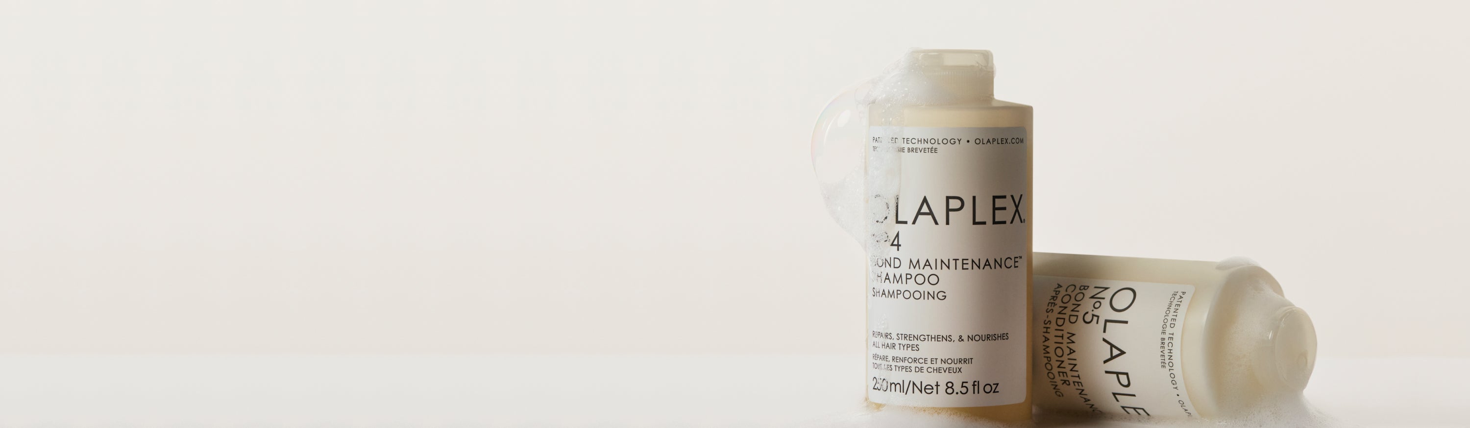bottle of olaplex shampoo standing up next to a sideways olaplex conditioner bottle with some suds