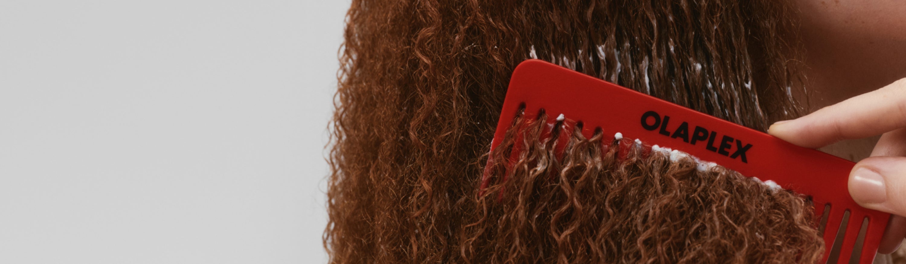 Image of girl with red curly hair using a red olaplex comb to brush it
