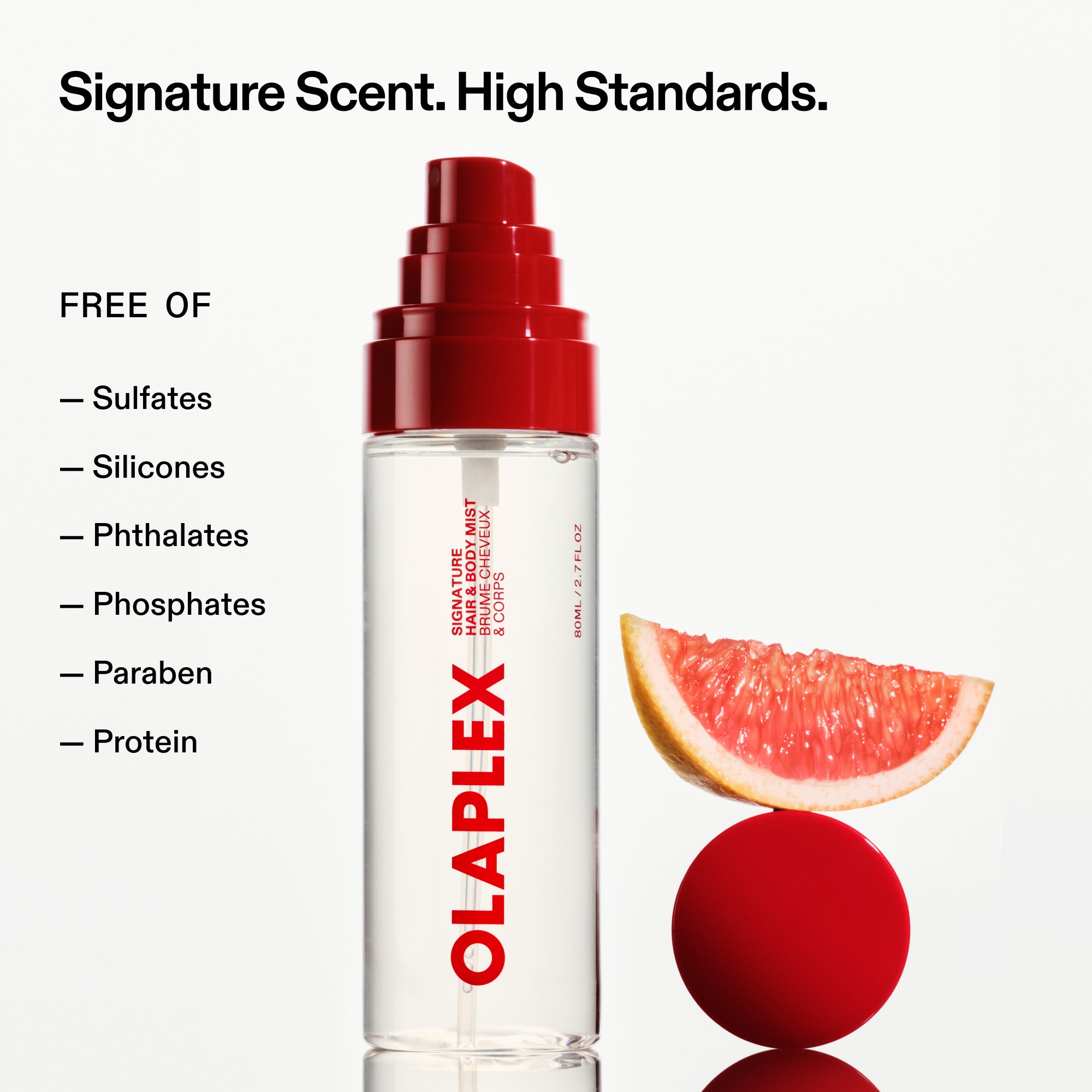An OLAPLEX hair and body mist bottle stands next to a grapefruit slice balanced on a red sphere. Text at the top reads, "Signature Scent. High Standards." A checklist on the left reads, "FREE OF: Sulfates, Silicones, Phthalates, Phosphates, Paraben, Protein.