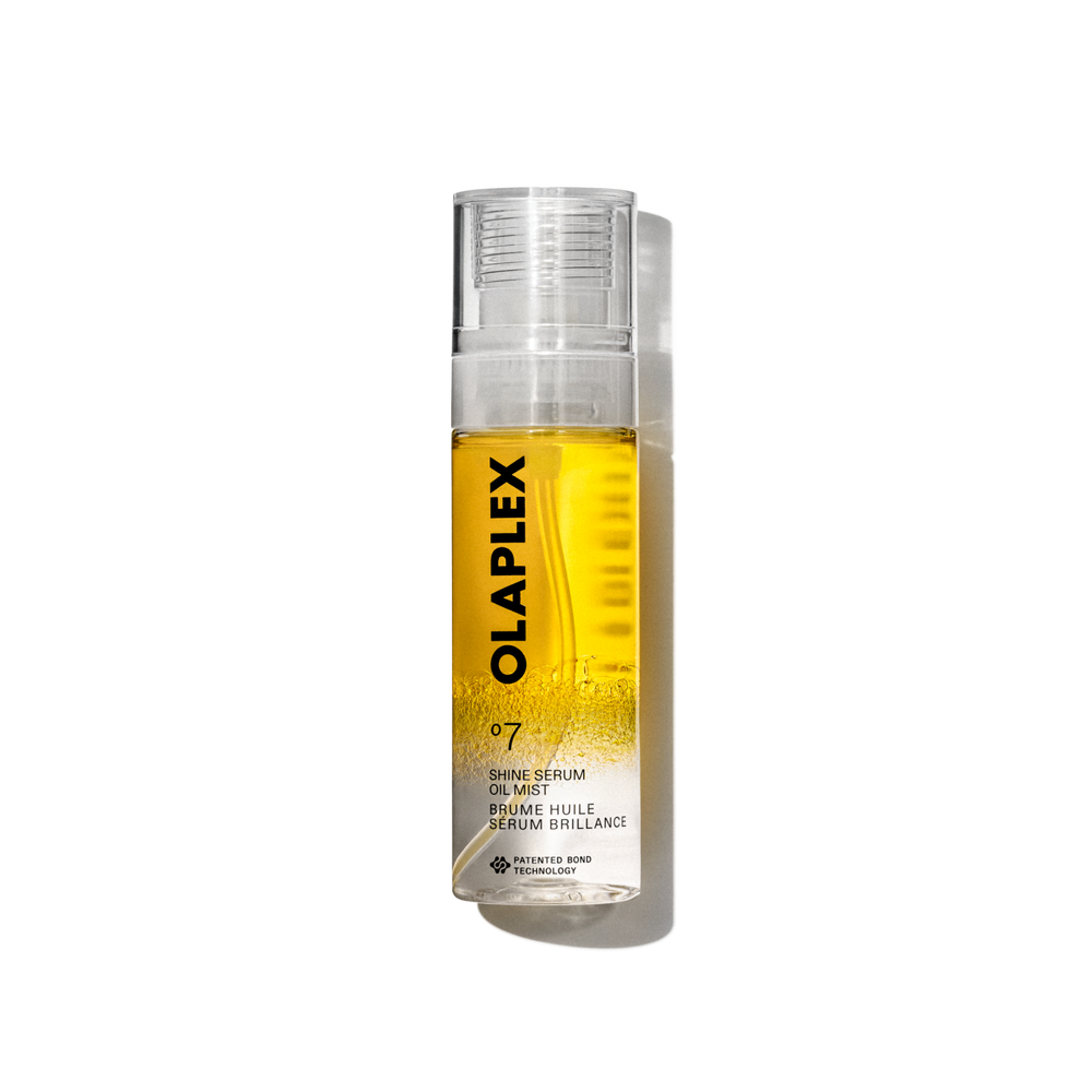 Photo du produit Olaplex N°.7 Shine Serum Oil Mist dans un flacon pulvérisateur transparent de 80 ml. Le flacon présente un liquide jaune vif visible à l'intérieur, un bouchon transparent, et une étiquette blanche épurée sur le bas avec un texte noir affichant le nom du produit, les détails et le logo signature "N°. 7". Le flacon est isolé sur un fond quadrillé transparent. - main view